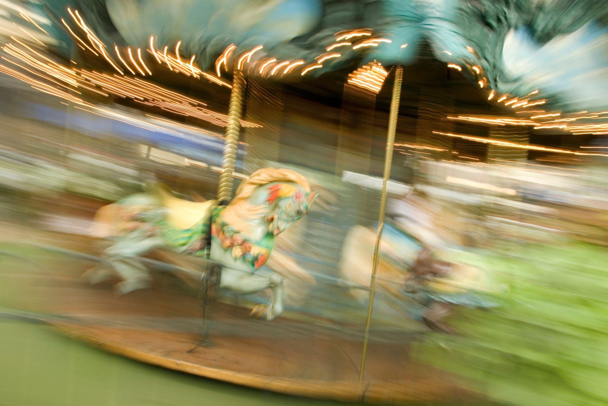 Blurred photograph of a carousel in motion with painted horses and glowing lights, creating a sense of movement and nostalgia.