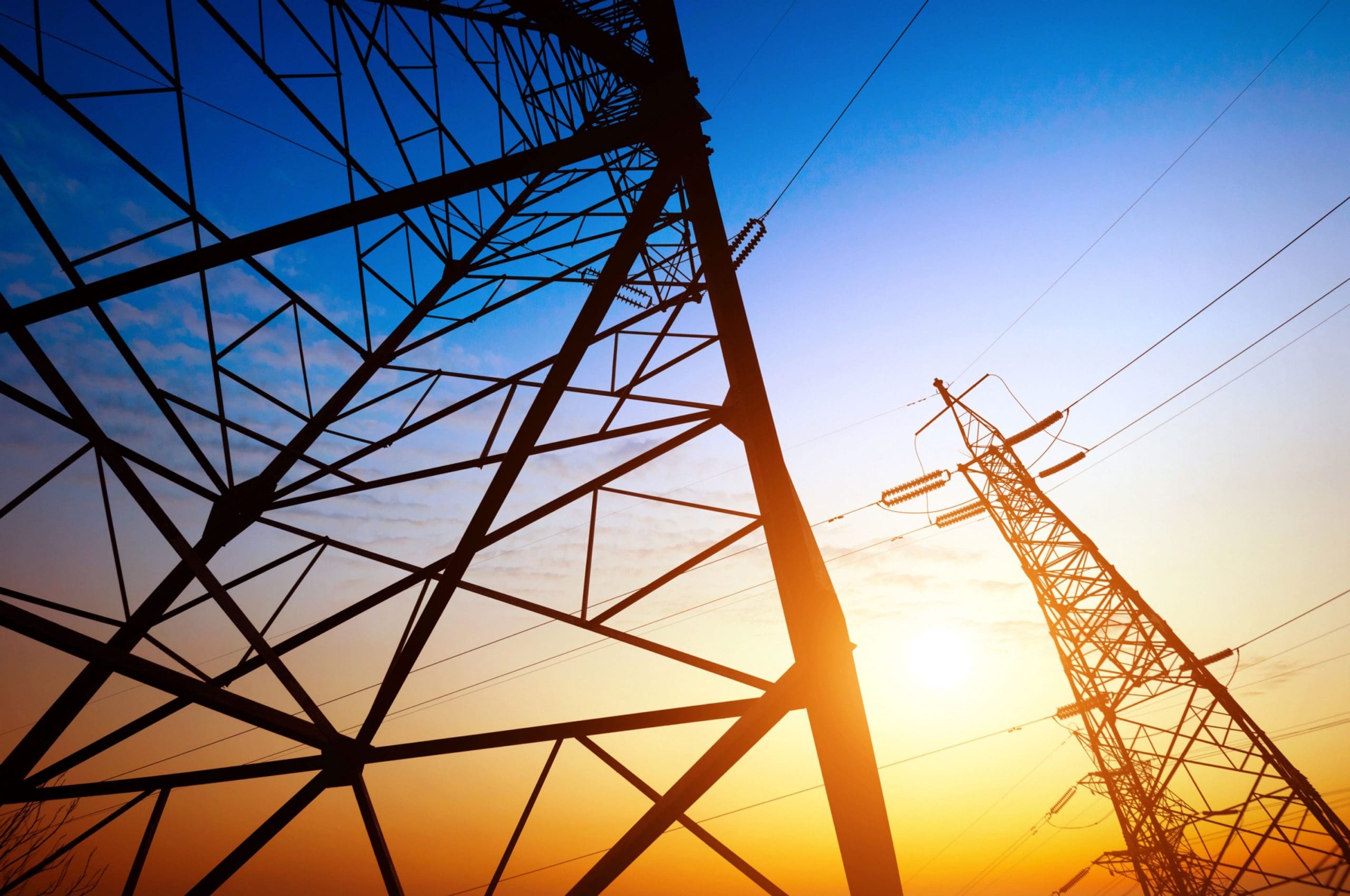 Silhouette of electricity pylons and power lines against a colourful sunset sky, representing energy and infrastructure.