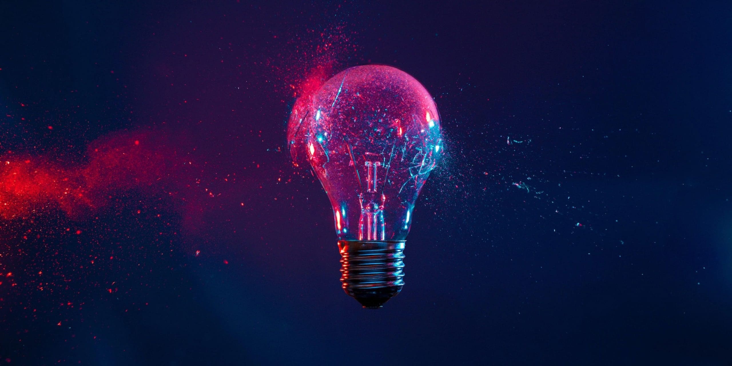 A glowing light bulb surrounded by red and blue particles against a dark background, symbolising creativity and innovation.