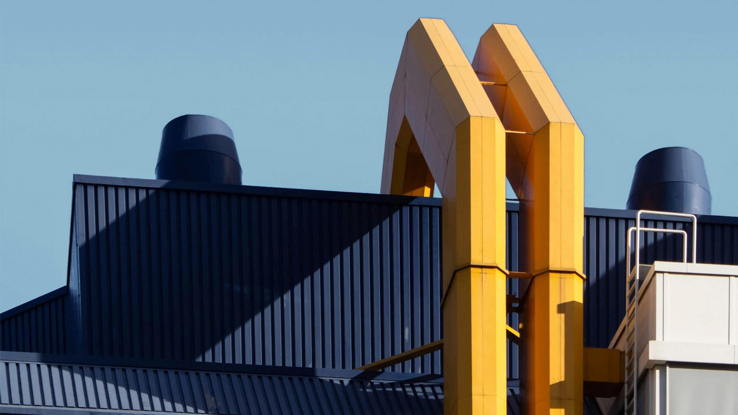 Modern architectural detail featuring a yellow metal structure on a dark blue industrial roof against a clear blue sky.