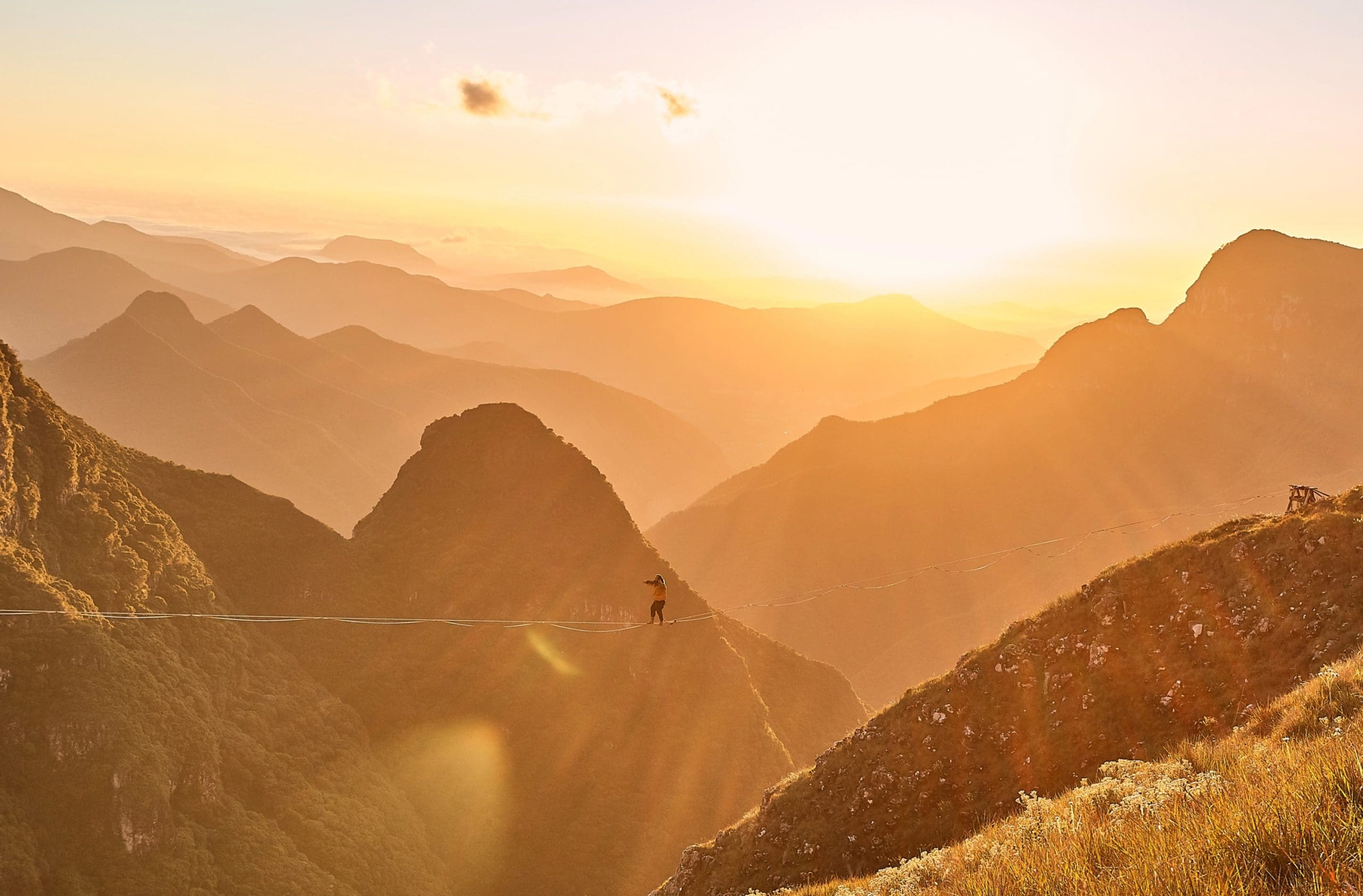 Person walking across a tightrope in between mountains at sunrise