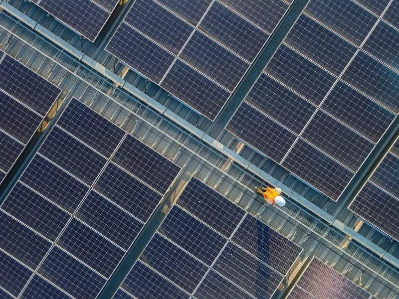 Overhead view of a worker in orange inspecting solar panel arrays.