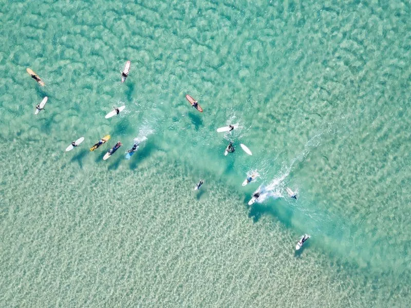 Group of surfers paddling and waiting in clear shallow water.