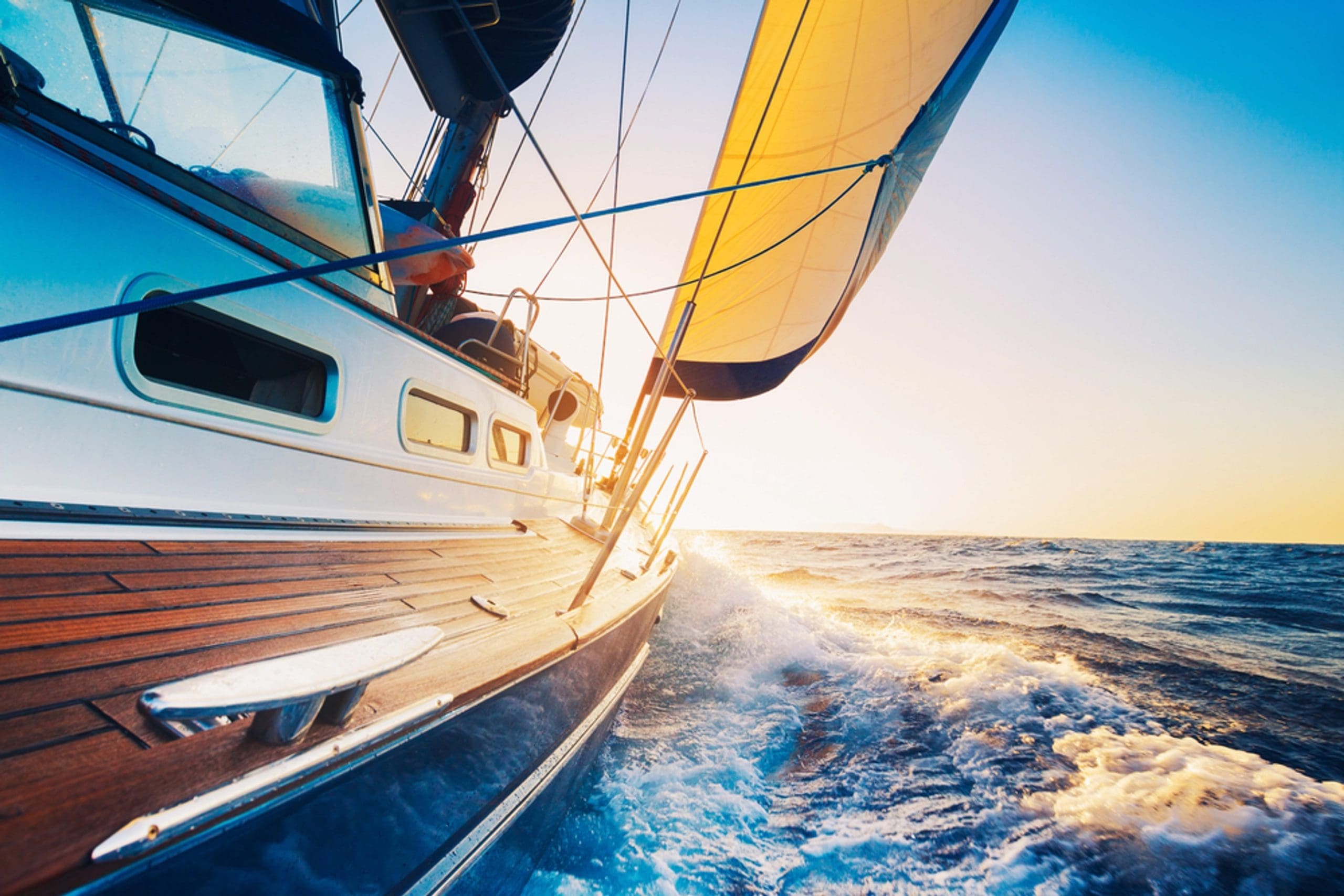 Image of sailboat on choppy water with the sun setting in background