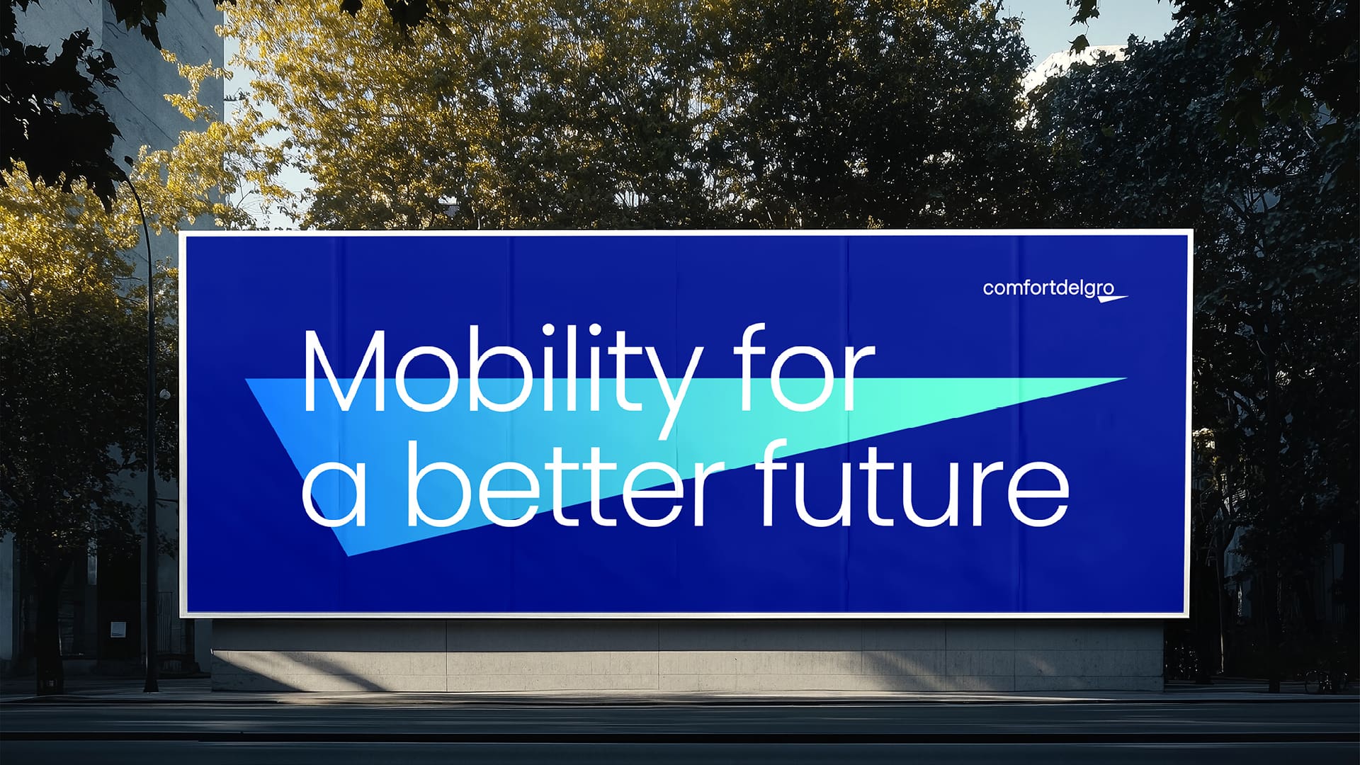 Large blue outdoor billboard reading “Mobility for a better future” with the ComfortDelGro logo, set along a tree-lined urban street in daylight.